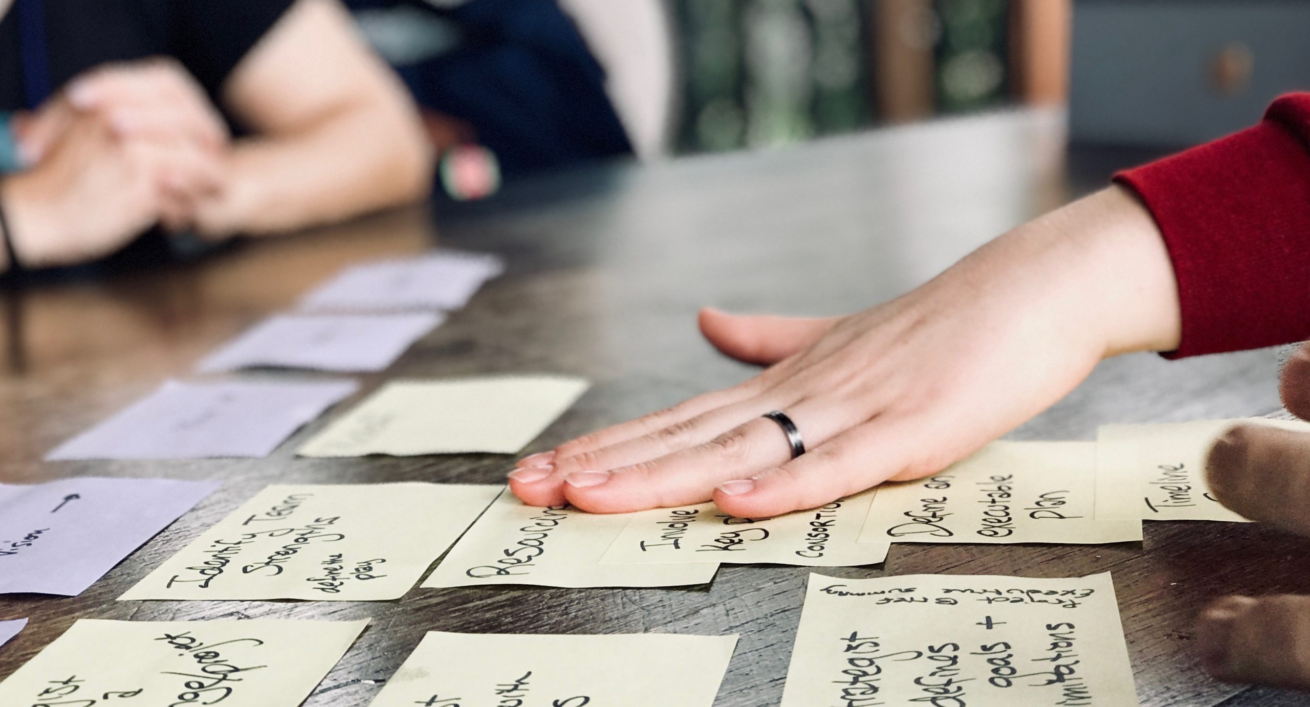 Sticky notes line a conference table. Someone is reaching out a hand toward one of the sticky notes.