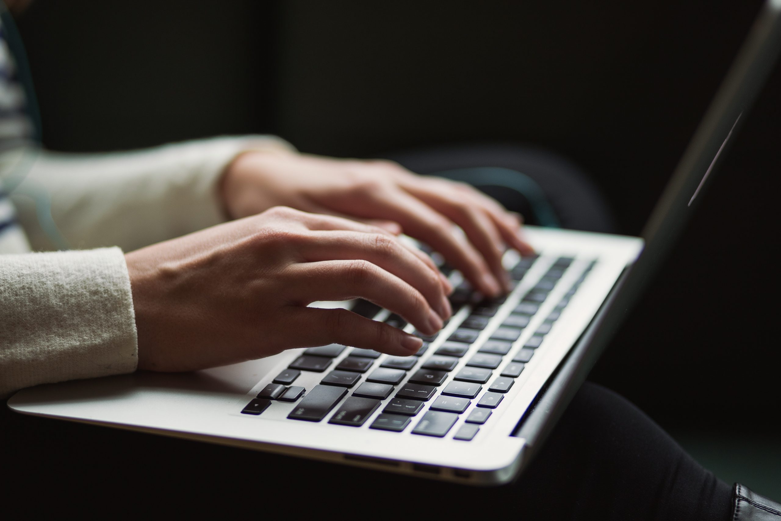A photograph of a person's hands typing on laptop computer keyboard.